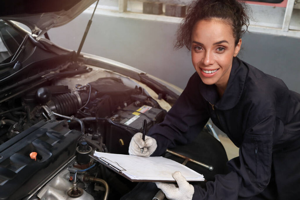 Kobieta mechanik samochodowy pracujący w garażu, mechanik samochodowy sprawdzanie i naprawa samochodu klienta w centrum serwisowym samochodu, koncepcja warsztatu samochodowego. - Zdjęcie, obraz