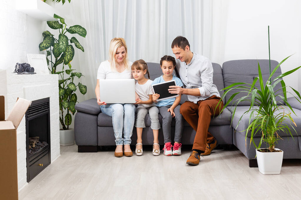 Νέοι χαρούμενη casual οικογένεια των δύο παιδιών και ζευγάρι κάθεται στον καναπέ και βλέποντας αστεία βίντεο ή κινούμενα σχέδια σε touchpad - Φωτογραφία, εικόνα