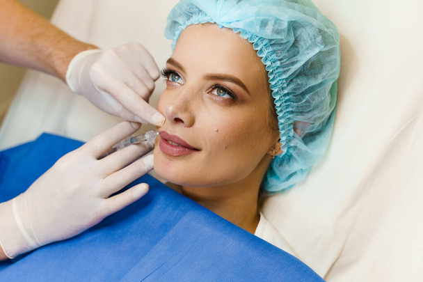 Close-up lippen augmentatie injecties voor aantrekkelijk meisje. Plastisch chirurg injecteert in de lip in een medische kliniek. Cosmetische verjongende gezichtsbehandeling. Lege ruimte voor advertenties - Foto, afbeelding