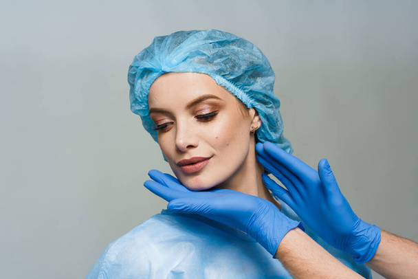 Consultation with plastic surgeon on white background. Cosmetic rejuvenating facial treatment. Doctor man with blue medical gloves touches girl face. Patient ask about lips and chin injections - Foto, Imagem
