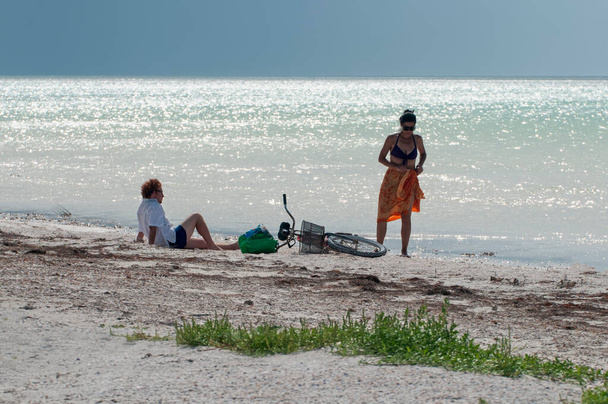 Un jeune couple inconnu assis au bord de la mer avec un vélo à Holbox Island, au Mexique. En arrière-plan la mer des Caraïbes et le ciel nuageux - Photo, image