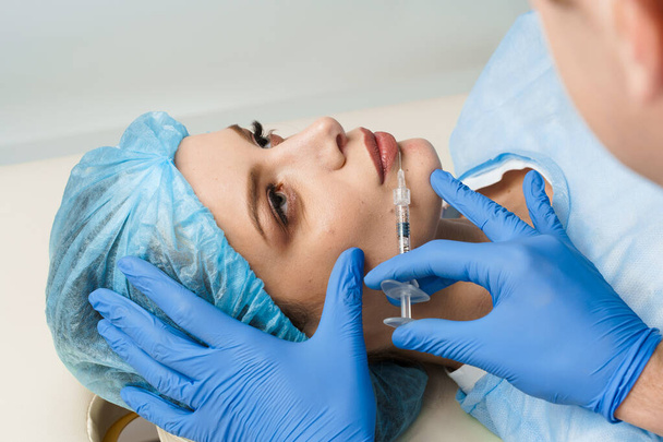 Lips augmentatie injecties voor aantrekkelijk meisje op witte achtergrond. Plastisch chirurg injecteert in de lip in een medische kliniek. Cosmetische verjongende gezichtsbehandeling. Lege ruimte voor advertenties - Foto, afbeelding