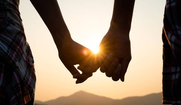 Aşk ve Sevgililer Günü konsepti. Gün batımında el ele tutuşan bir çift, aşkın ve mutlu ilişkinin sembolü.. - Fotoğraf, Görsel