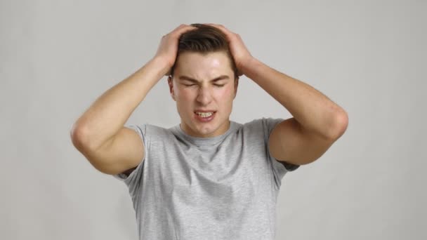 Young man suffering from headache attack, rubbing his aching head, grey studio background, slow motion - Footage, Video