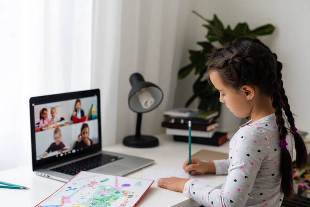 Маленькая девочка учится в Интернете, используя свой ноутбук дома - Фото, изображение