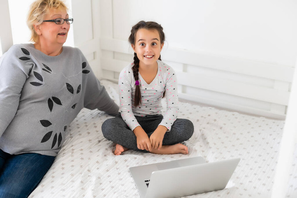 彼女の祖母とラップトップコンピュータを使用してかわいいと幸せな女の子の子供,オンラインeラーニングシステムを通して勉強. - 写真・画像
