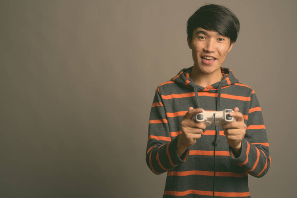 Молодий азіат грає в ігри проти сірого походження - Фото, зображення