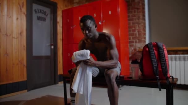 Afro-americano atletico giovane si pulisce la faccia con un asciugamano nello spogliatoio - Filmati, video