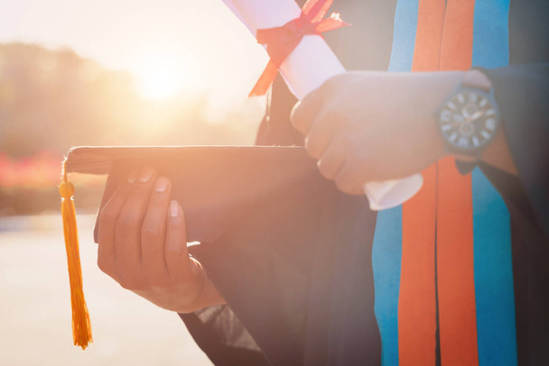 Επιλεκτική και κοντινή εστίαση ενός απόφοιτου πανεπιστημίου κατέχει πιστοποιητικό πτυχίου και το καπέλο αποφοίτησης γιορτάζει στην τελετή αποφοίτησης. - Φωτογραφία, εικόνα