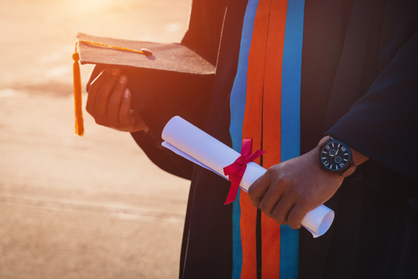 Επιλεκτική και κοντινή εστίαση ενός απόφοιτου πανεπιστημίου κατέχει πιστοποιητικό πτυχίου και το καπέλο αποφοίτησης γιορτάζει στην τελετή αποφοίτησης. - Φωτογραφία, εικόνα