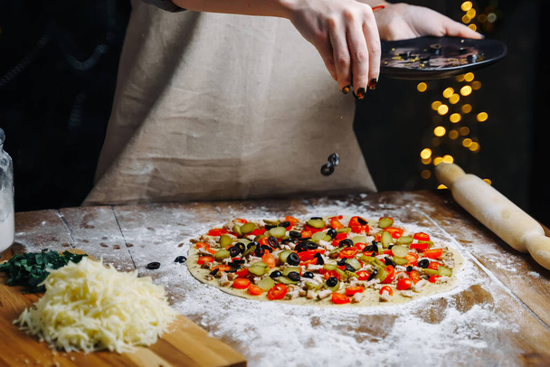 Cucina della pizza fatta in casa. Donna cuocere a mano versando le olive fette sulla pasta. Concetto di preparazione degli alimenti in quarantena a causa di epidemia. - Foto, immagini