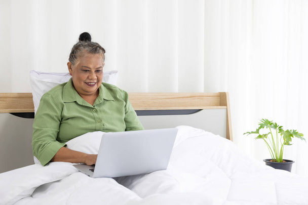 senior vrouw met laptop op bed thuis - Foto, afbeelding