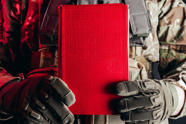 Photo d'un soldat en uniforme tenant un livre rouge fermé vue rapprochée. - Photo, image