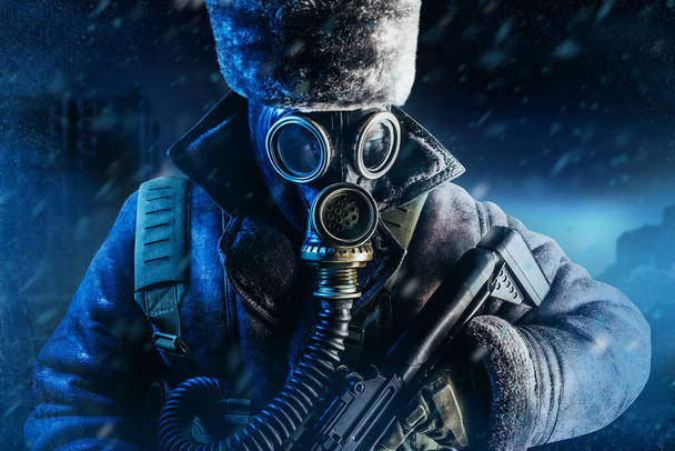 Photo of winter stalker soldier in fur coat, hat standing with pouch vest, gas soviet mask and rifle in stormy snowfall weather. - Photo, Image
