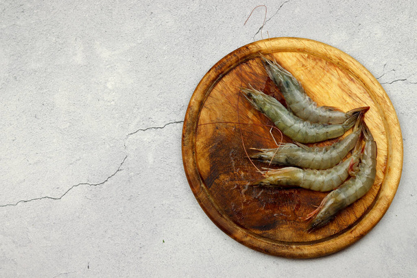 Raw prawns served on a wooden board  on a light wooden background. Top view, flat lay - Foto, imagen