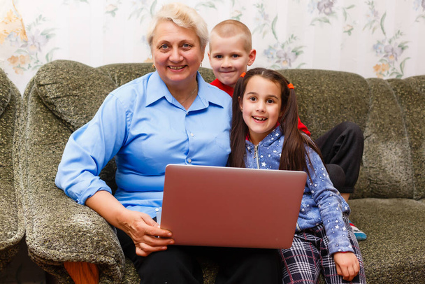 Grand-mère avec petits-enfants utilisant un ordinateur portable à la maison - Photo, image
