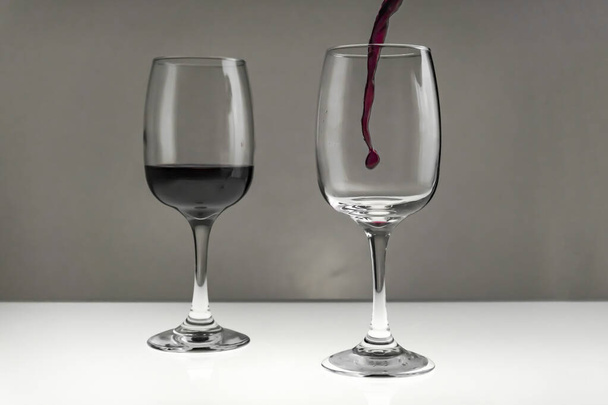Red wine is poured from a bottle into a glass on a blurred background, close-up.  - Foto, Bild
