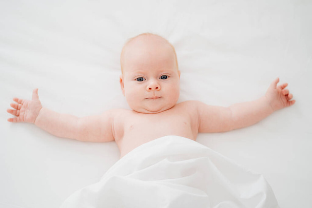 cute red-haired baby lies on a white bed. concept of baby care - Foto, Imagem