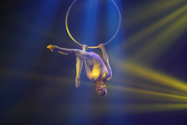 Flexible young woman make performance on aerial hoop, flexible back on aerial hoop, aerial circus show, yellow light. Flexible woman gymnast upside down on hoop. Show in night club - Photo, Image