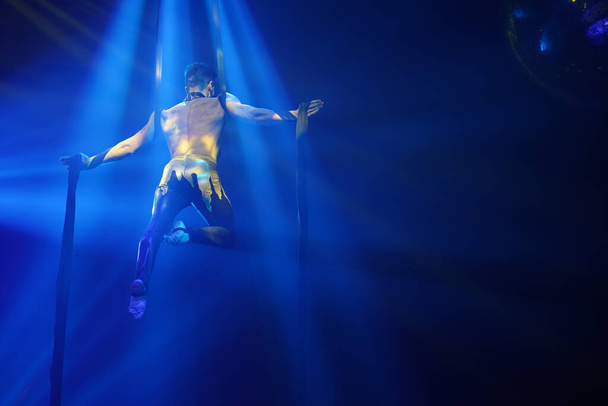 Brasileiro forte sexy homem fazer desempenho em sedas aéreas em luzes azuis. Treinamento desportivo ginásio e conceito de estilo de vida. Fundo preto - Foto, Imagem
