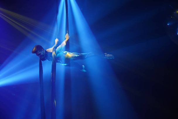 Brezilyalı güçlü seksi adam mavi ışıklarda hava ipekleriyle performans sergiliyor. Spor salonu ve yaşam tarzı konsepti. Siyah arkaplan - Fotoğraf, Görsel