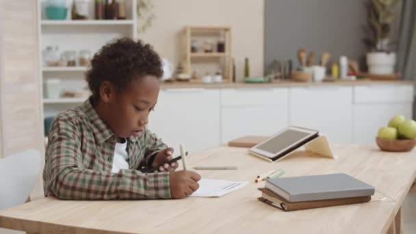 Brustbild eines afroamerikanischen Schuljungen, der zu Hause am Schreibtisch sitzt, Test macht, mit Smartphone betrügt, Mutter kommt, Gerät vom Sohn nimmt, ihn schimpft und geht - Filmmaterial, Video