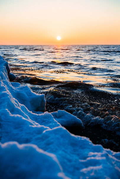 Színes naplemente. Hóval borított tengerpart egy napos téli napon. Hideg hullámok a Balti-tenger felett, Lettország - Fotó, kép