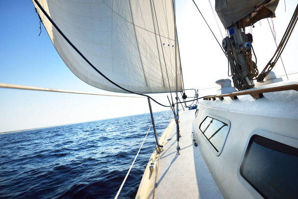 Fehér jacht vitorlázás egy napos nyári napon. Közelkép a fedélzetről az orrra és a vitorlákra. Hullámok és vízcsobbanások. Tiszta kék ég. Balti-tenger, Svédország. Szállítás, sport, szabadidős tevékenység - Fotó, kép
