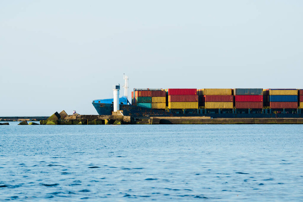 Büyük bir kargo konteynırı gemisi yaklaşıyor. Arka planda deniz feneri var. Baltık Denizi, Letonya - Fotoğraf, Görsel