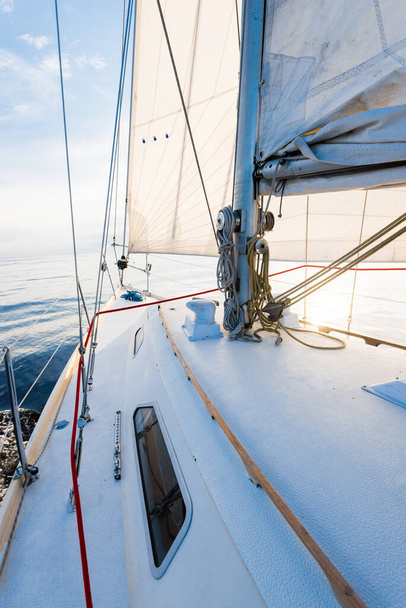 Blanco balandra yate aparejado navegando cerca de la costa de Maine, Southwest Harbor, EE.UU.. Una vista desde la cubierta a la proa, mástil y velas. Cielo azul oscuro, rayos de sol a través de las nubes - Foto, imagen