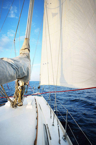 白いヨットは日没時に静かな水の中を航海する。デッキから弓、マスト、帆への眺め。見事な雲景だ。自然鏡だ。スポーツとレクリエーションのテーマ。バルト海,ラトビア - 写真・画像