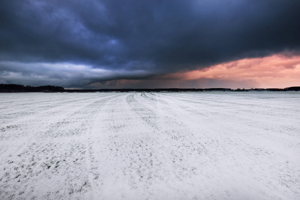 Hóval borított szántott szántóföldek traktornyomokkal. Drámai naplemente, színes felhők. Téli táj. Lettország. Meleg tél, éghajlatváltozás, globális felmelegedés - Fotó, kép