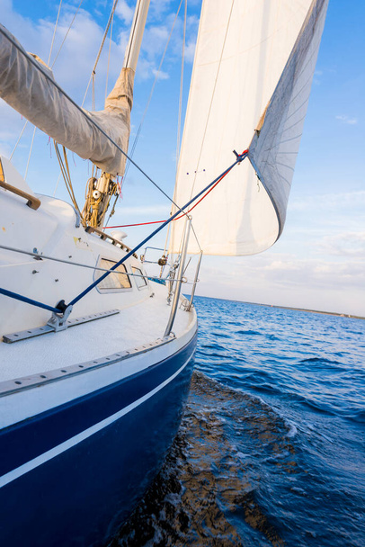 ノルウェーの日没時に川を航行する青いヨット。デッキから弓と帆への眺め。真っ青な空。スポーツとレクリエーションのテーマ - 写真・画像