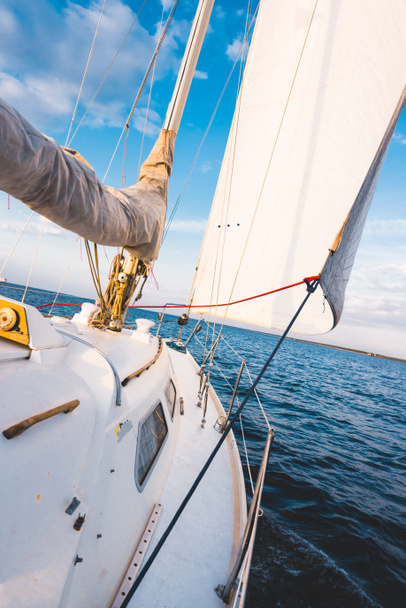 Weiße Jacht segelt in einem stillen Wasser bei Sonnenuntergang. Blick vom Deck auf Bug, Mast und Segel. Atemberaubende Wolkenlandschaft. Naturspiegel. Thema Sport und Erholung. Ostsee, Lettland - Foto, Bild