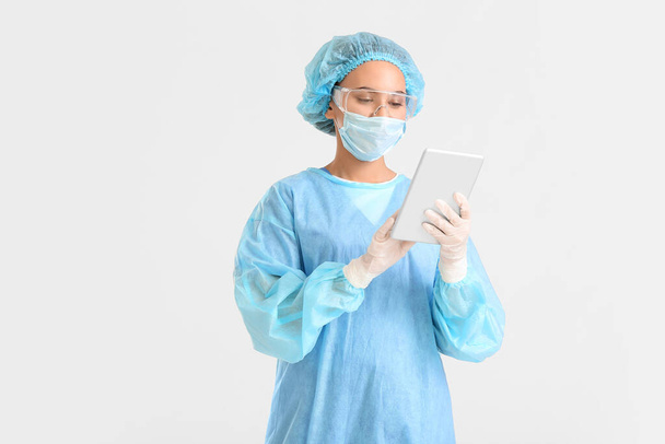 Portrait of female surgeon with tablet computer on light background - Foto, Imagen
