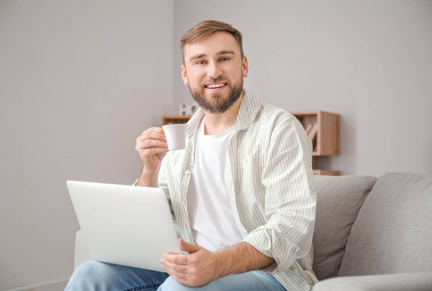 Młody człowiek z laptopem pijący gorącą kawę w domu - Zdjęcie, obraz
