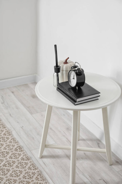 Table with books, alarm clock and decor near white wall - Photo, Image