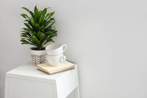 Zimmerpflanze, Notizbücher und Tassen auf Tisch neben Lichtwand - Foto, Bild