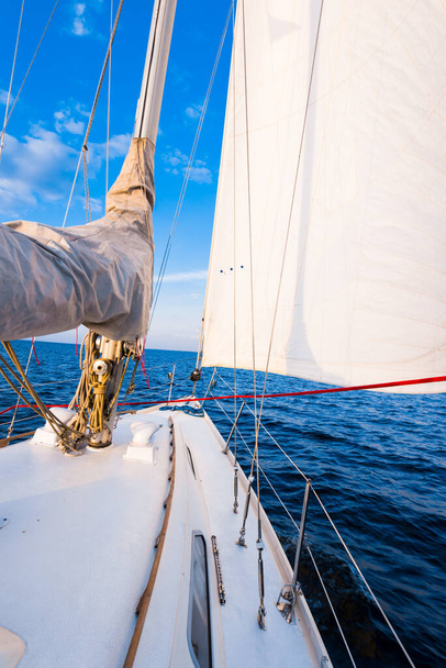Weiße Jacht segelt in einem stillen Wasser bei Sonnenuntergang. Blick vom Deck auf Bug, Mast und Segel. Atemberaubende Wolkenlandschaft. Naturspiegel. Thema Sport und Erholung. Ostsee, Lettland - Foto, Bild