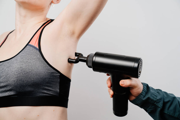 Η γυναίκα χρησιμοποιεί όπλο για μασάζ. ιατροαθλητική συσκευή.  - Φωτογραφία, εικόνα