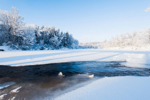 Gefrorener Fluss und schneebedeckter Wald nach einem Schneesturm im morgendlichen Dunst. Strahlend blauer Himmel. Winterwunderland. Gauja-Nationalpark, Sigulda, Lettland - Foto, Bild