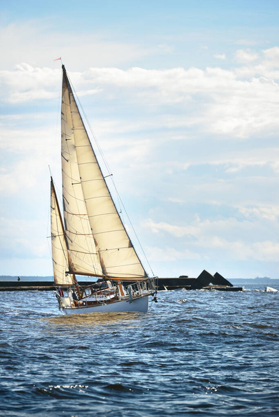 Ročník bílá dřevěná plachetnice pluje za oblačného dne. Maják v pozadí - Fotografie, Obrázek
