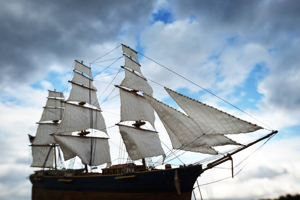 Antikvariátní dřevěný model clipper vysoké lodi, detailní záběr. Dramatická obloha, tmavé bouřkové mraky. Tradiční řemeslo, suvenýr, koníček, sběr, vinobraní, modelování. Koncept nulového odpadu - Fotografie, Obrázek