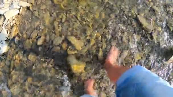 Girl walking barefoot on stones of shallow river close-up, sunny summer day - Footage, Video