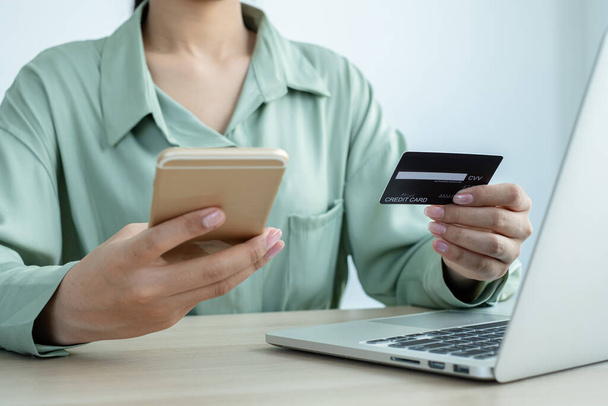 Το χέρι της επιχειρηματία κατέχει μια πιστωτική κάρτα και χρησιμοποιώντας ένα smartphone για online αγορές και πληρωμή στο διαδίκτυο στο γραφείο. - Φωτογραφία, εικόνα