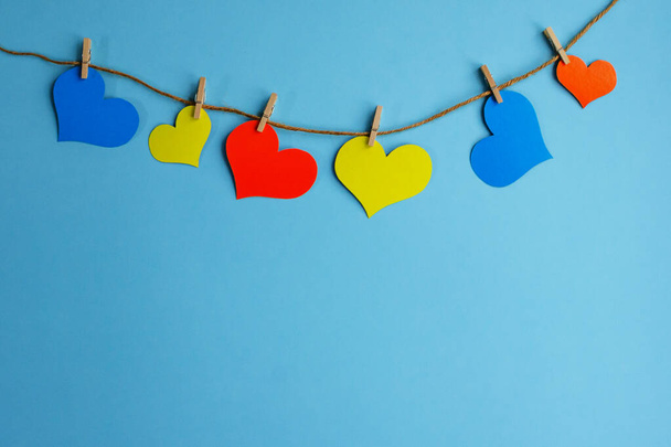 Colored hearts with clothespins hang on a clothesline on a blue background with copy space. Valentines day concept, flat lay. - Foto, afbeelding