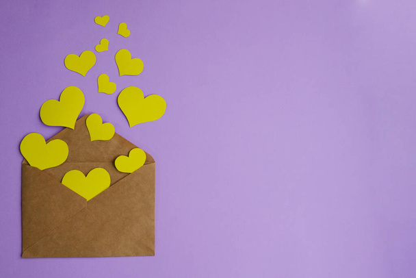 Brown envelope with yellow hearts on a lilac background with copy space. Flat lay, valentines day concept - Photo, Image