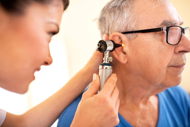 Doctor using otoscope to check on elder mans ear, nursing home medical doctors concept - Фото, изображение