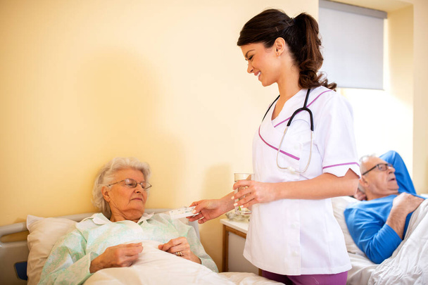 Caring young female doctor bringing glass of water to her patient in a nursing facility - Foto, immagini