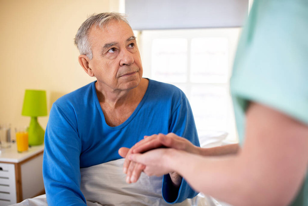 Caring nurse holding a hand of a senior man occupant in a nursing home room, providing care for the elder concept  - Fotó, kép